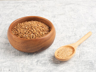 Buckwheat in a wooden cup, salt in a spoon on a white concrete background