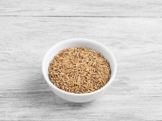 Spice cumin in ceramic bowl on white wooden background