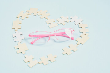 childish pink glasses and a heart made of wooden puzzles on a blue background, glasses for small children