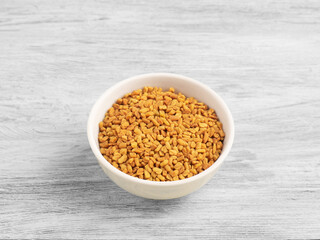 Spice black fenugreek in ceramic bowl on white wooden background