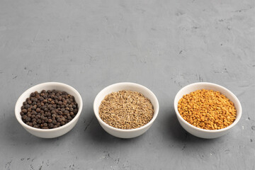Spice black pepper, fenugreek, cumin in ceramic bowls in row on a gray concrete background