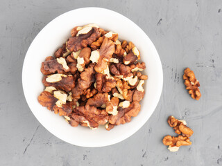 Shelled walnuts in ceramic bowl on gray concrete background