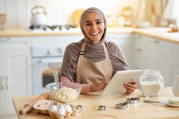 Cooking Blog. Happy Muslim Woman in Hijab Using Digital Tablet In Kitchen