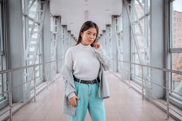 brunette with a Japanese appearance in a light sweater and a gray jacket and jeans against the backdrop of the city