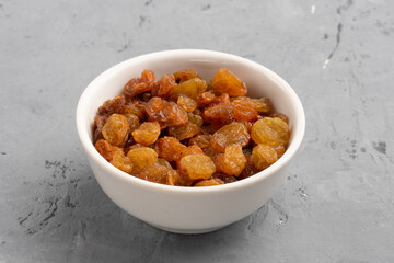 Raisins in a white bowl on gray concrete background