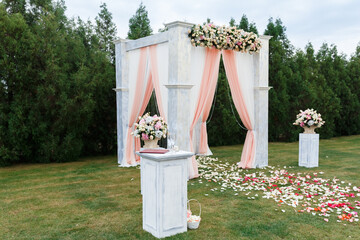 Place for wedding ceremony in white color .White square wedding arch with bouquets of pastel roses in the forest.