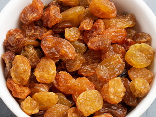 Raisins in a white bowl on gray concrete background