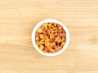 Raisins in a white bowl on brown wooden background