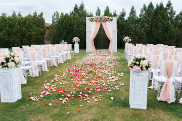 Place for wedding ceremony in white color .White square wedding arch with bouquets of pastel roses in the forest.