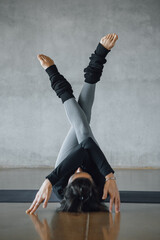 Fit young woman coach practices individual hatha yoga on a black mat in a white background, pilates...