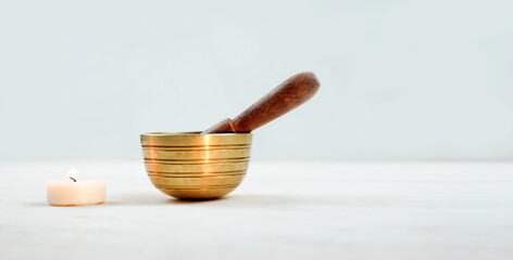 Tibetian singing bowl with candle on white wooden background, sound therapy. Copy space