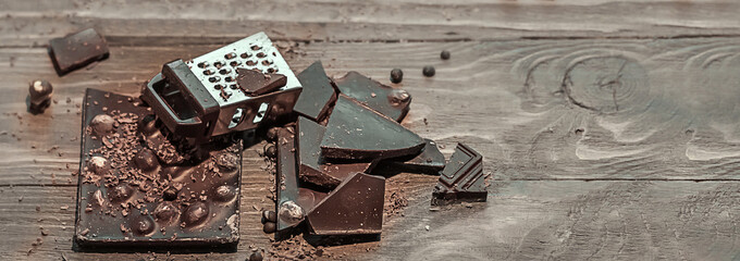Composition of bars and pieces of various dark chocolate, cups of cocoa with grated chocolate, hazelnuts on a brown wooden background. Close-up, top view, copy space.Banner