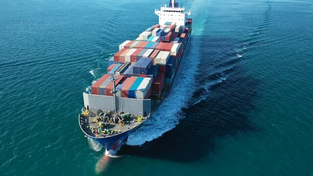 Aerial drone rotational video of Container cargo Ship carrying load in truck-size colourful containers in deep blue open ocean sea 