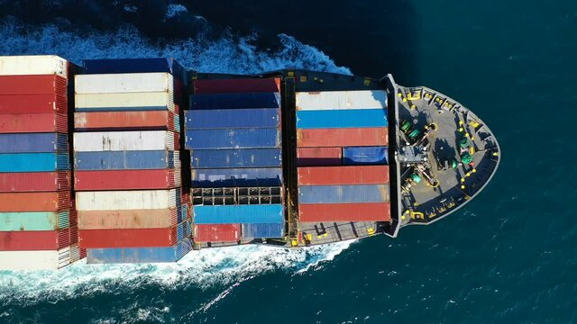 Aerial top down video over Container cargo Ship carrying load in truck-size colourful containers in deep blue open ocean sea 