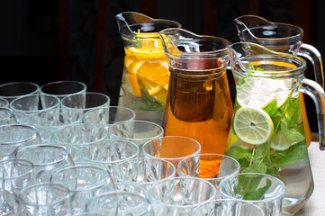 On the table there are many glasses and jugs with natural drinks made from lemon and mint, oranges...