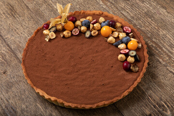Chocolate tart decorated with fresh berries and cape gooseberry on wooden table