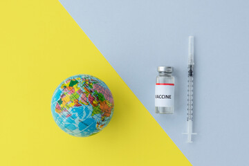 Top view of toy glose, vial with vaccine, and syringe on background from colors of 2021, yellow and...