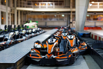 Kart cars parked one by one on indoor go-kart racing track in anticipation of drivers. Shallow focus. - obrazy, fototapety, plakaty