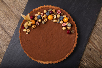 Chocolate tart decorated with fresh berries and cape gooseberry on black slate