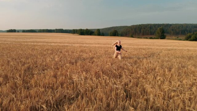 Happy young girl runs across field, touching ears of wheat with her hand. Beautiful free woman enjoying nature in warm sunshine in a wheat field on sunset background. girl travels.