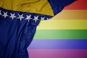 waving national flag of bosnia and herzegovina on a gay rainbow flag background.