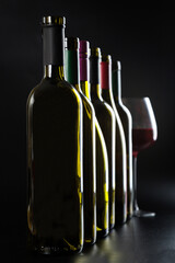 several different bottles of wine and a glass with red wine on a dark glossy background.