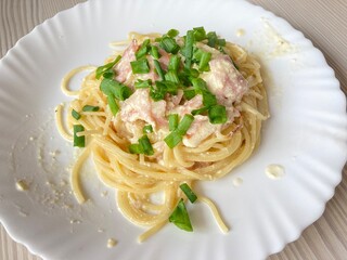pasta carbonara with fresh herbs lies on a white plate top view, cooking at home