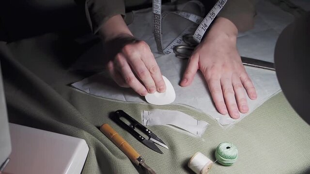 A dressmaker in a sewing workshop takes a pattern, at night, close-up. Women's hands trace the pattern with chalk on the fabric. Sewing process in the studio. Slow motion