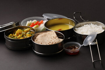 Typical Stainless steel Lunch Box or Tiffin with Maharashtrian food menu Chapati OR Roti, Plain Dal Tadka, White Rice Potato sabji with salad and pickle