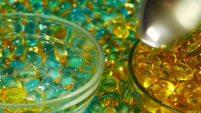 Yellow gelatin capsules are scooped out with a spoon. Yellow capsules of fish oil are placed in a glass bowl on a blue background. Omega 3 Gold Fish Oil Capsules. High quality 4k footage