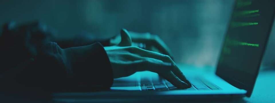 Female Hacker working on laptop at night in the modern workspace. Female Hands are typing a code at keyboard or hacking a website.