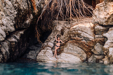 Beautiful girl in black bikini swimming suit posing near the rocks at the sea