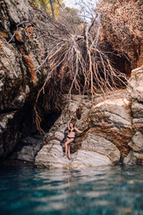 Beautiful girl in black bikini swimming suit posing near the rocks at the sea