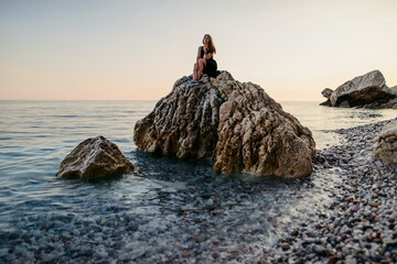 Girl in black dress posing at sunset on the rock at sea