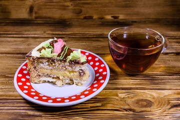 Cup of tea and plate with slice of Kiev cake with cream, nuts and meringue on a wooden table