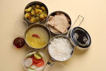 Typical Stainless steel Lunch Box or Tiffin with Maharashtrian food menu Chapati OR Roti, Plain Dal Tadka, White Rice Potato sabji with salad and pickle