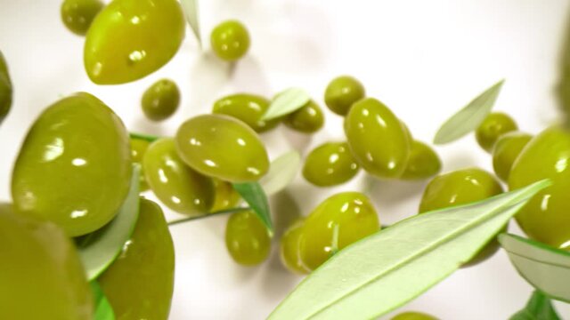 Super Slow Motion Shot of Falling Fresh Green Olives and Leaves on White Background at 1000 fps.