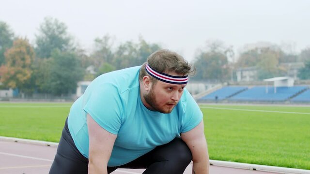 Obese charismatic man in the stadium get ready to start running he is at starting line preparing for a hard marathon