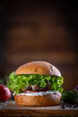 Craft beef burger with cheese, lettuce, tomato and sauce on wooden background