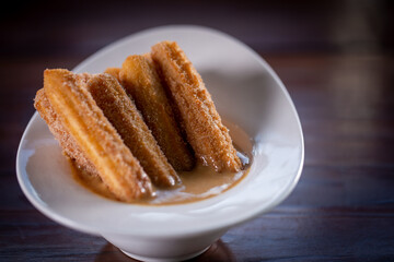 Churros sticks with caramel in a wooden background