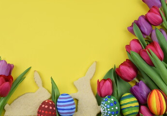 tulips, painted eggs and bunny shaped cookies on yellow background 
