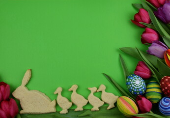 tulips, painted eggs and chick and bunny shaped cookies on green background 