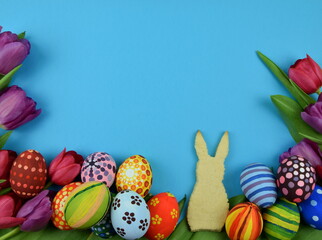 tulips, painted eggs and bunny shaped cookies on blue background 