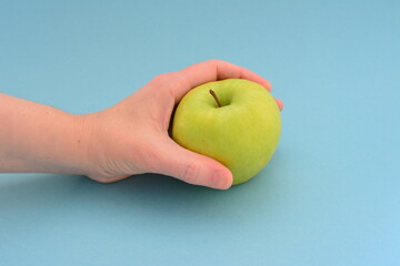 woman's hand holding green apple on the blue background