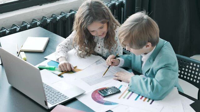Little business people looking at office papers, discussing solving a problem, having conversation. Little children businesswoman and businessman working in office with diagrams 