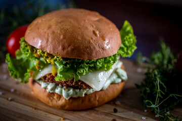Craft crispy chicken burger with cheese, lettuce, tomato and sauce on wooden background