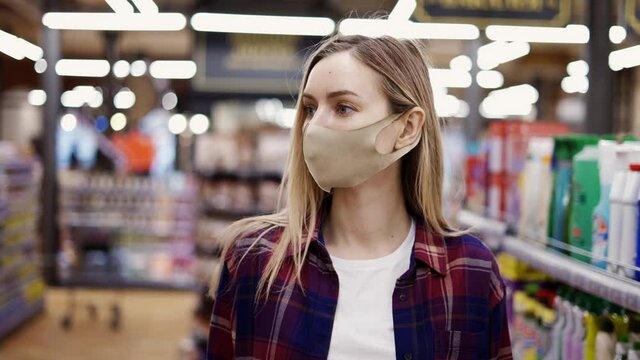 Woman in protective mask walking by supermarket between aisles, looking for something