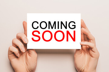 Female hands hold card paper with text COMING SOON on a yellow background. Business and finance concept