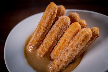 Churros sticks with caramel in a wooden background