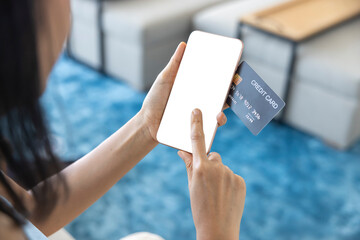 A woman shopping online on her sofa at home with a smartphone using a black credit card. And use your finger to tap the screen to verify the identity. Concept about business. Photo over shoulder shot.